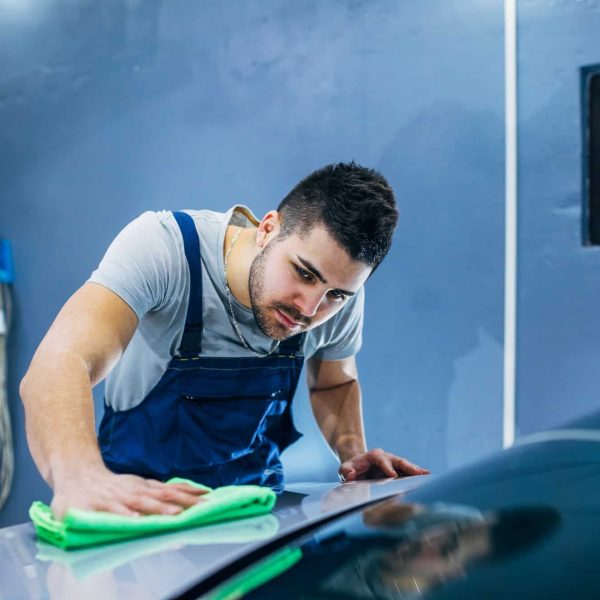 A man in an apron wiping down the hood of a car.