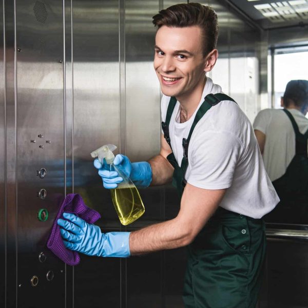 A man in blue gloves cleaning the inside of an elevator.